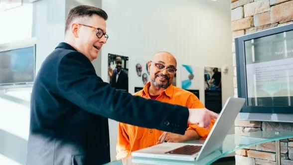 Coach training employee, using laptop.