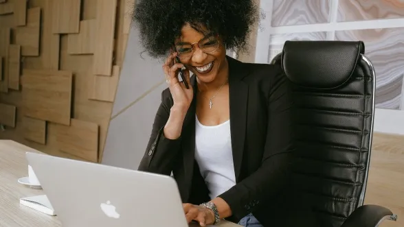 Women talking on phone happily, facing laptop